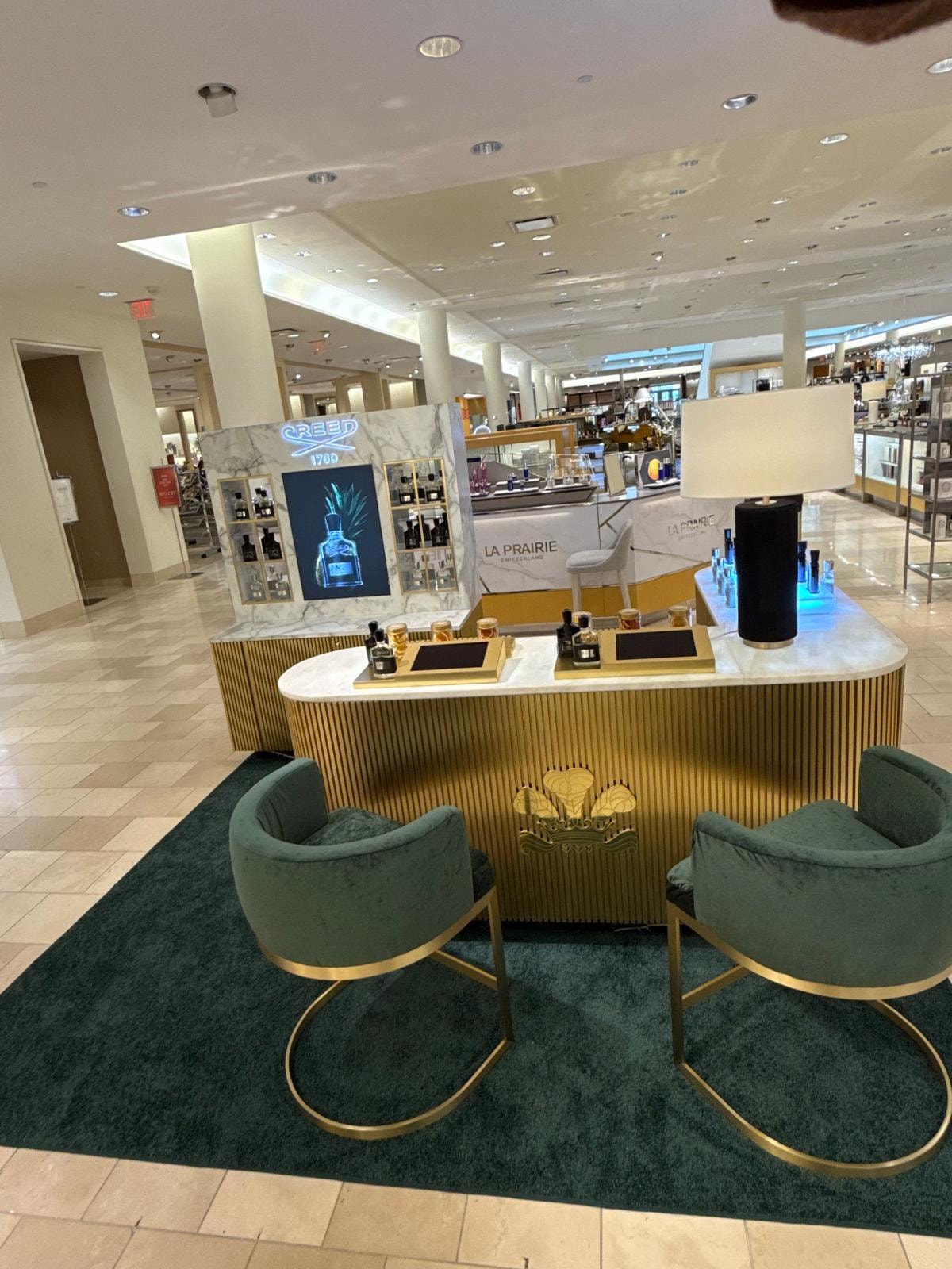 Creed 1760 luxury fragrance counter with gold ribbed panels, marble top, and green velvet seating